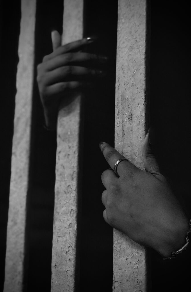 Close-up of a woman's hands gripping prison bars, with the hope captured in black and white.