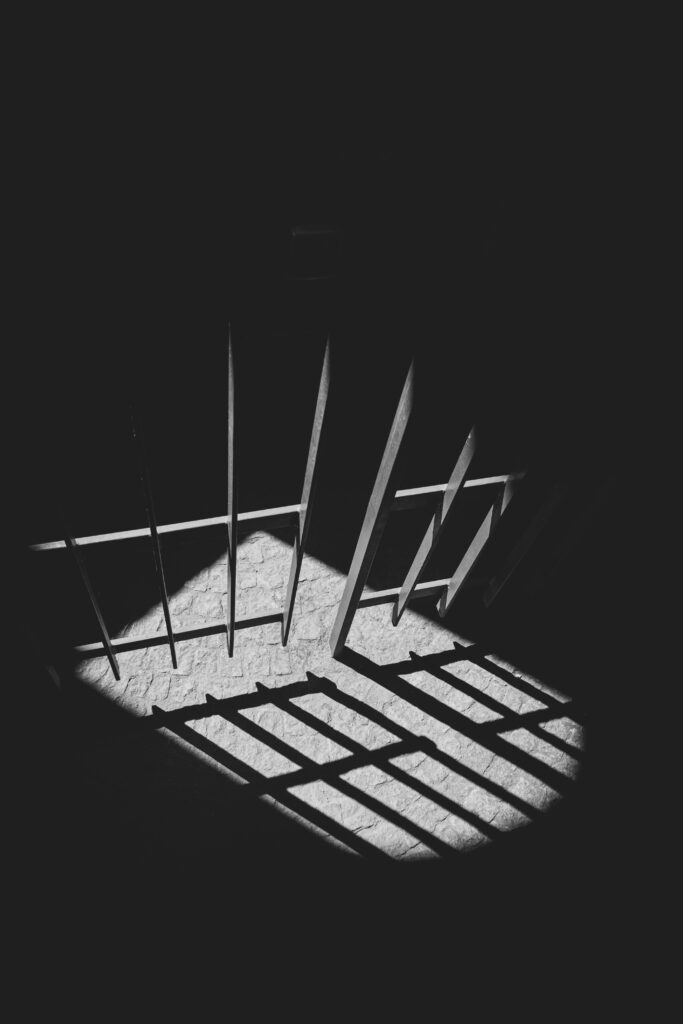 Shadow of prison bars cast on the floor in a dark, empty cell, symbolizing isolation, confinement, and life behind bars.